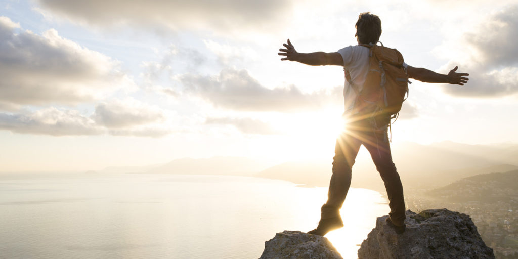 Man stands between boulders on summit, arms out